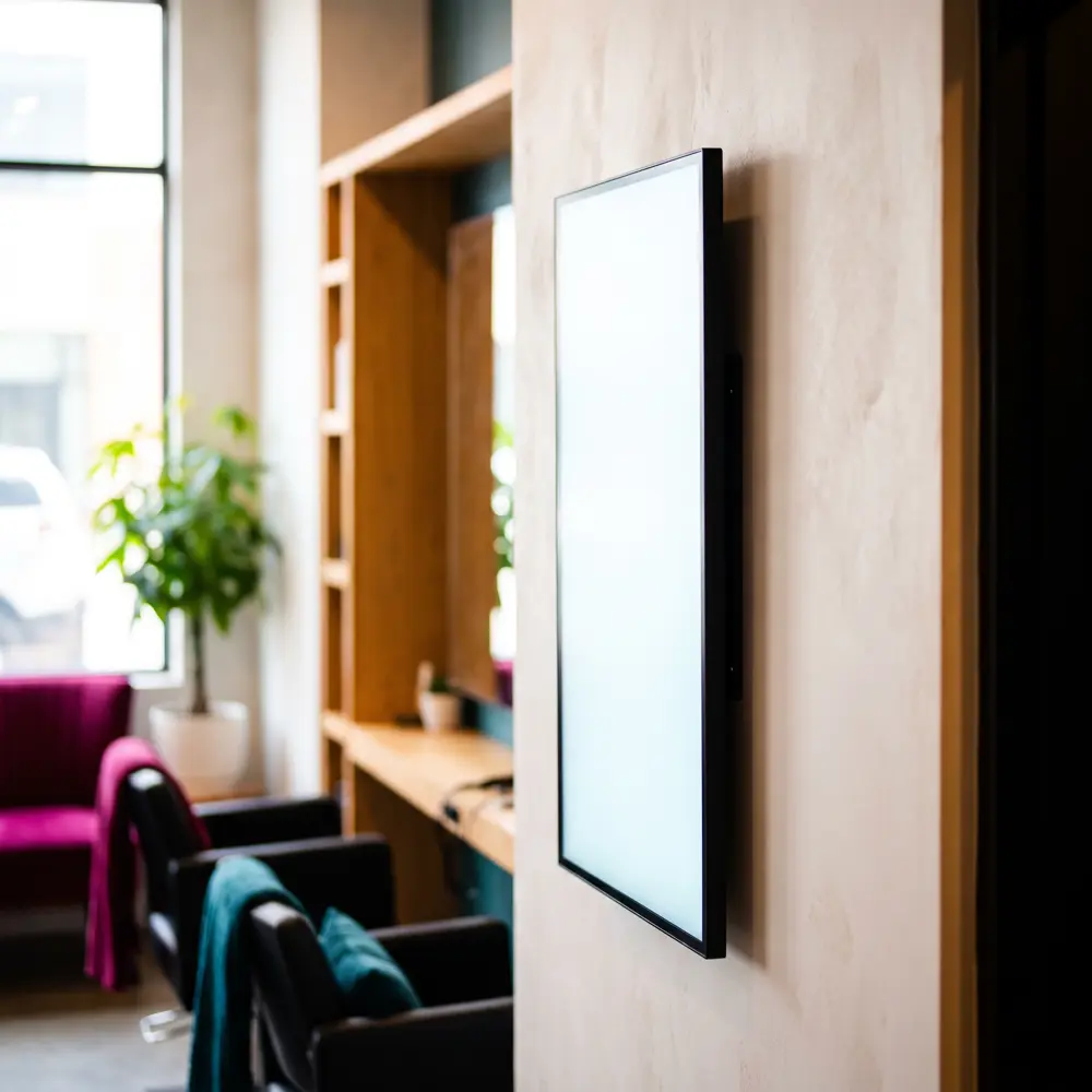 Schlanker digitaler Werbescreen im Hochformat, bündig an der Wand eines Salons montiert, ohne sichtbare Kabel.